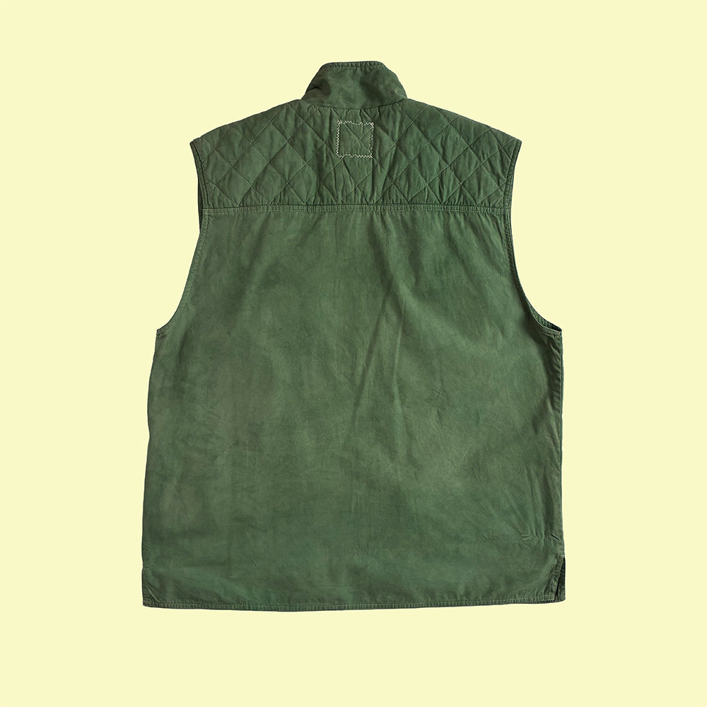 An hand dyed green quilted sleeveless gilet shown from the back, laid flat against a pale yellow background.