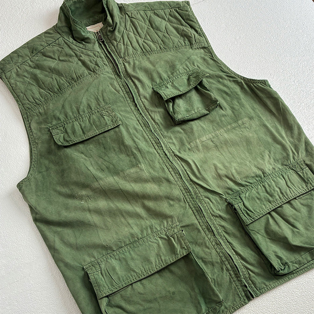 A hand dyed green quilted utility gilet with a front zipper and multiple flap pockets, laid flat on a light textured background.