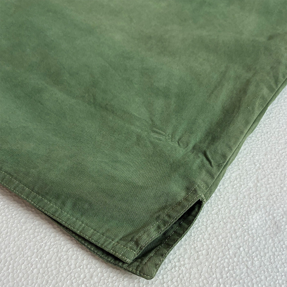 A close-up of an olive green gilet showing the texture and hem detail on a white textured background.