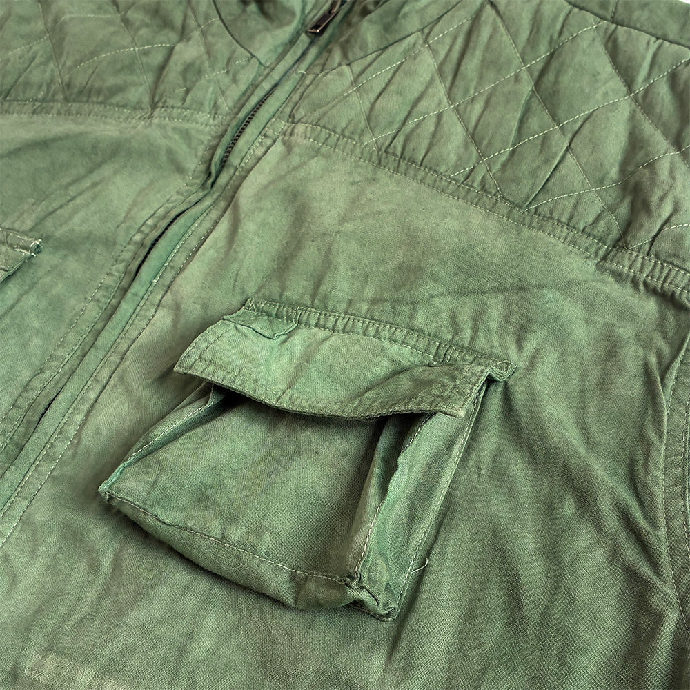 Close-up of an green quilted gilet with a diagonal zip closure and a flap pocket.