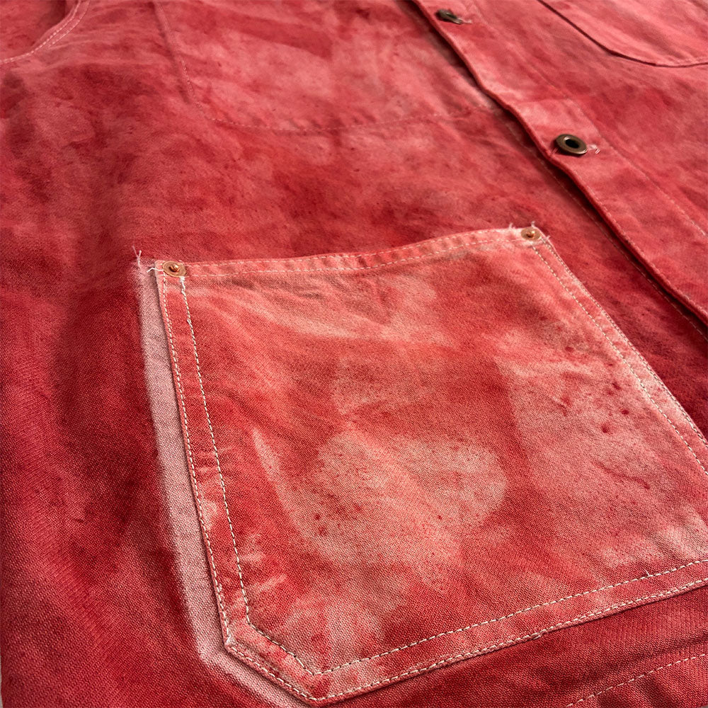 Close-up of a red chore jacket with a faded, distressed finish and a front patch pocket.