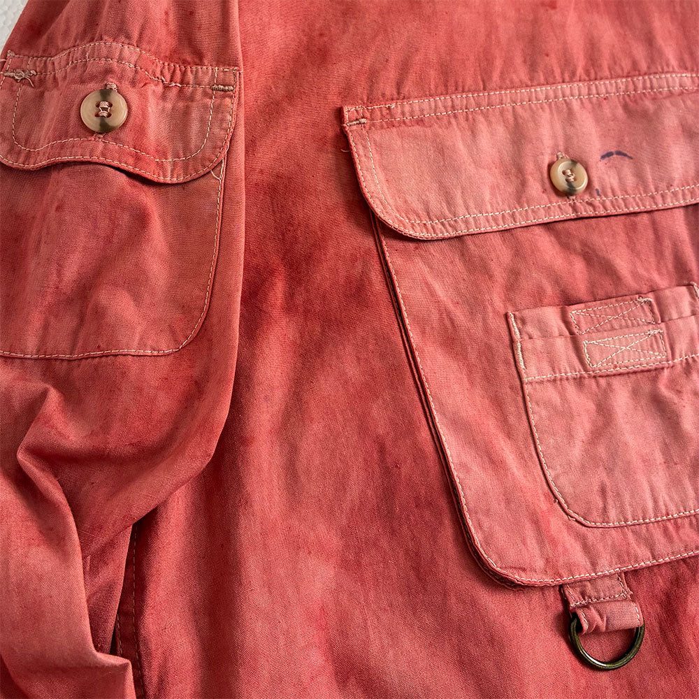 Close-up of a red and pink utility shirt with buttoned flap pockets and a metal ring detail on the sleeve.