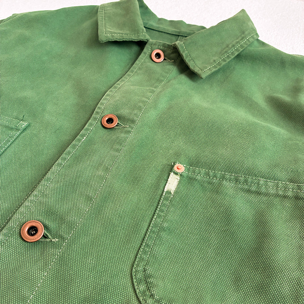 A close-up of a green canvas weave button-up shirt showing the collar, front button placket with copper-colored buttons, and a chest pocket.