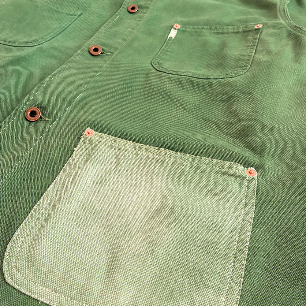 Close-up of a green canvas work shirt with a large front patch pocket, a chest pocket, and copper-toned metal snap buttons.